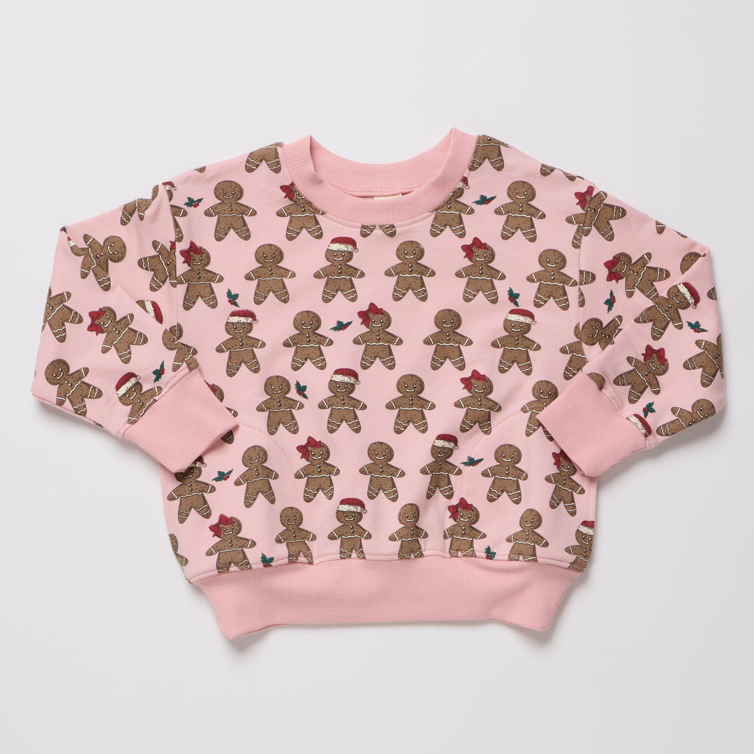 A pink crewneck sweatshirt with an all-over print of gingerbread cookies, some wearing red Santa hats, displayed flat against a light gray background.