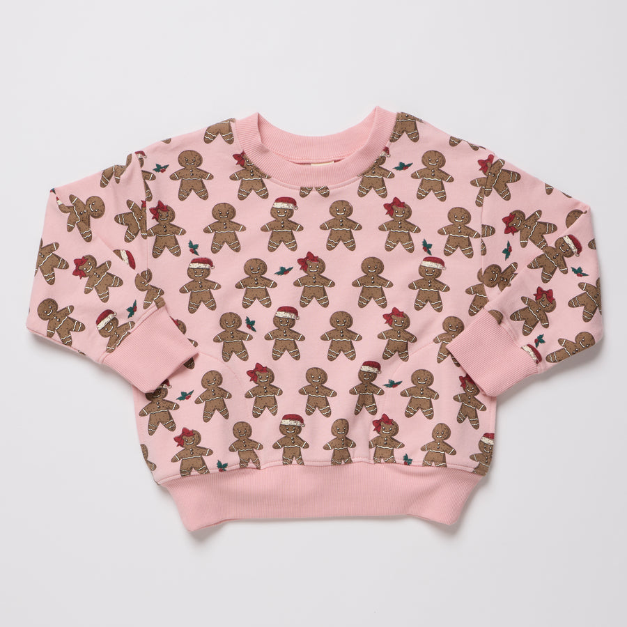 A pink crewneck sweatshirt with an all-over print of gingerbread cookies, some wearing red Santa hats, displayed flat against a light gray background.