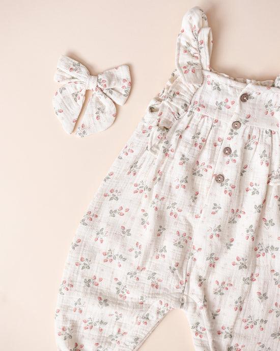 baby girl romper, beige fabric with tiny strawberries all over it. 4 buttons at the top of the romper. 