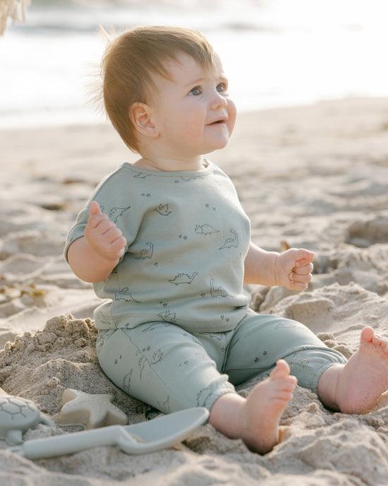 small baby wearing the 2 piece set with dinos printed all over it. 