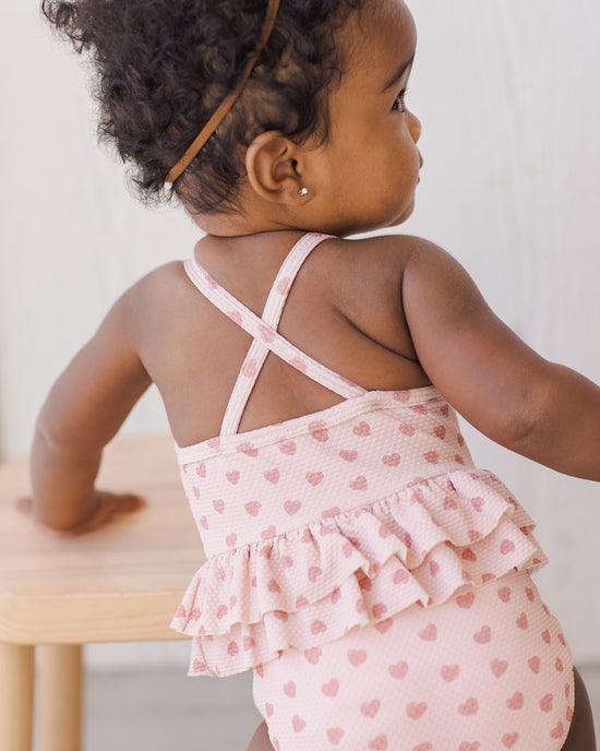 baby girl modeling the hearts peplum swimsuit from the back with the criss cross straps. 