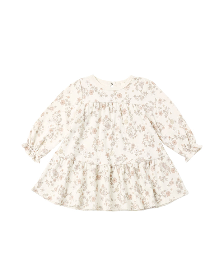 A long-sleeve baby dress with a tiered ruffle hem, featuring a delicate beige and brown floral pattern on a warm cream background.
