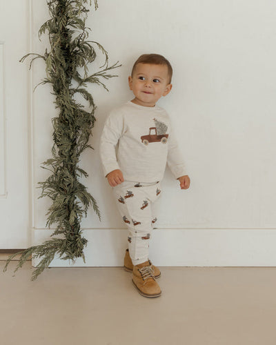 child modeling the 2 piece holiday set with red truck with a tree in the back. 