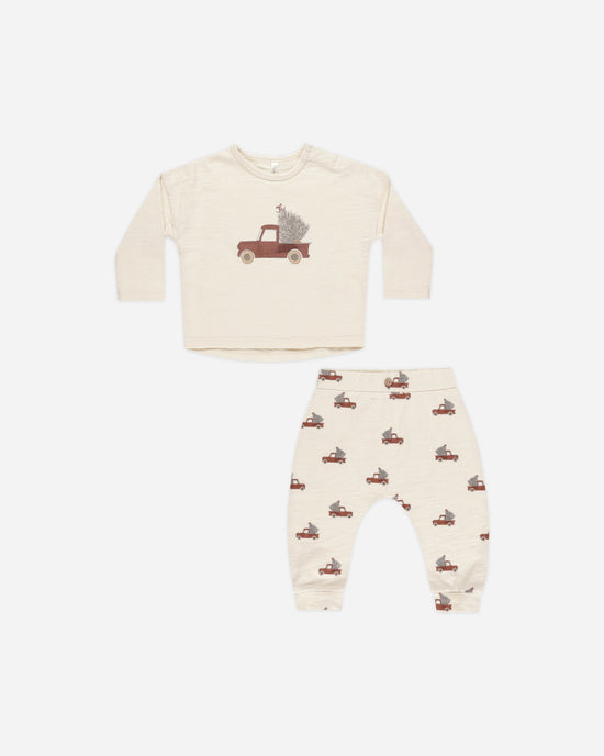 2 piece holiday set, beige in color with long sleeve top and pants. top has a bigger picture of a red pick up truck with a tree in the back. the truck and tree are smaller all over the pants. 