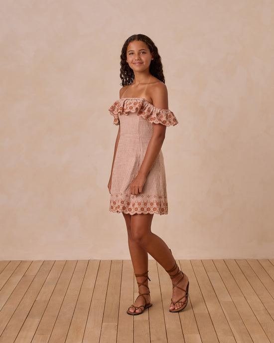 young girl modeling a red gingham dress with ruffle at the neckline and bottom of dress. the sleeves can be worn on the shoulder or off the shoulder as shown here. 