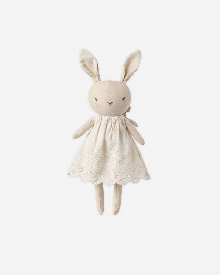 A cream-colored fabric bunny plush toy wearing a matching embroidered dress, centered on a light gray background.