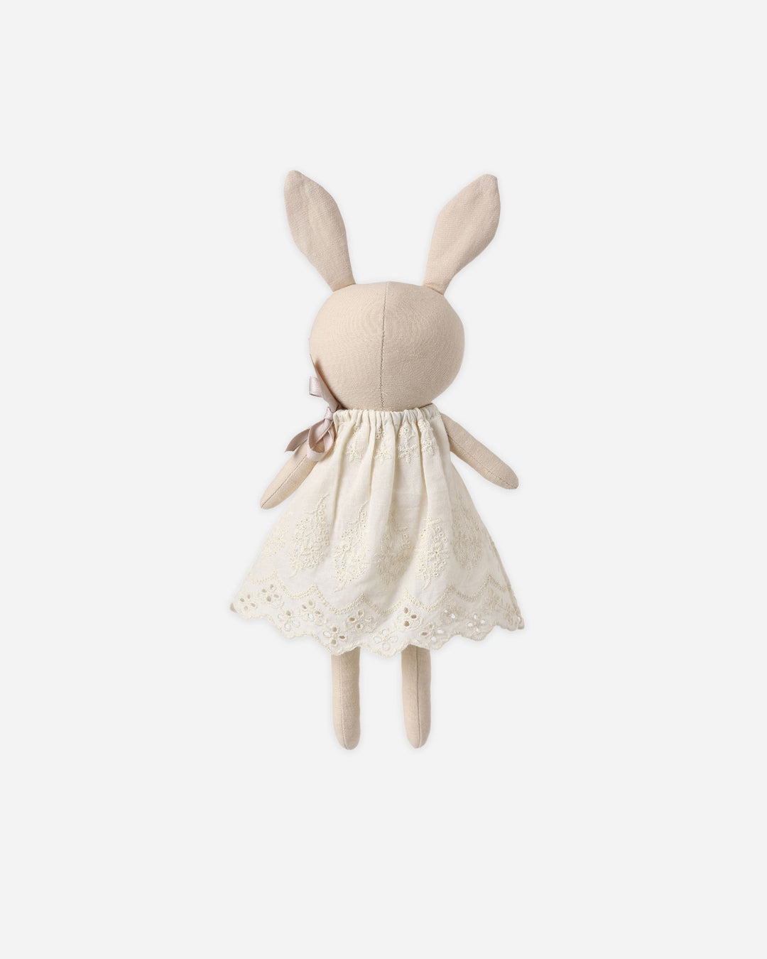 A plush bunny doll viewed from the back, wearing a cream-colored embroidered dress with a lace hem and a small bow on the back, set against a solid light gray background.