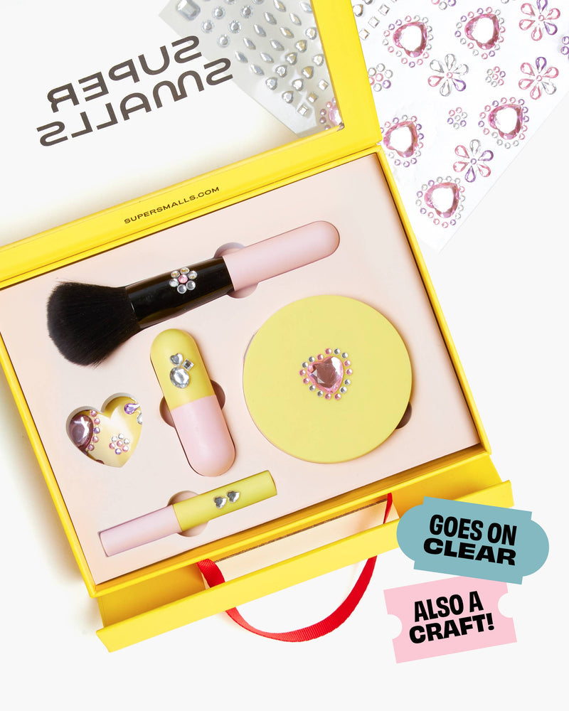 pretend make up kit with blush brush, conmpact, mascara and lipstick in light pink containers in a yellow packaging box.