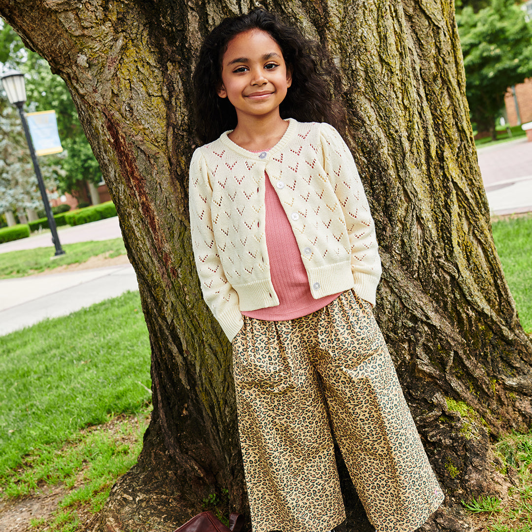 Young girl standing next to a tree in a park wearing wide leg leopard pants 