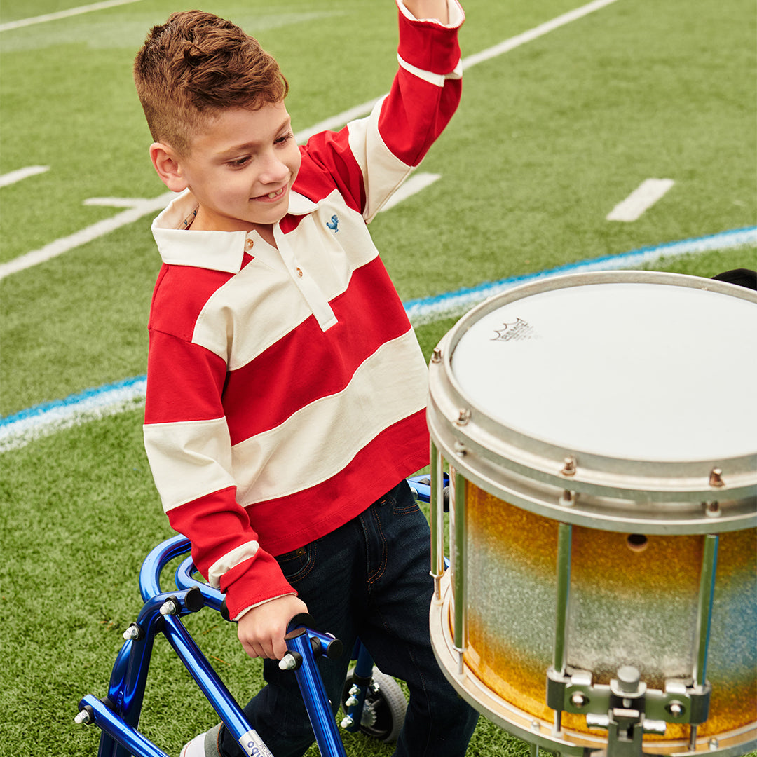 Child in a red and white striped shirt playing a drum on a grassy field
