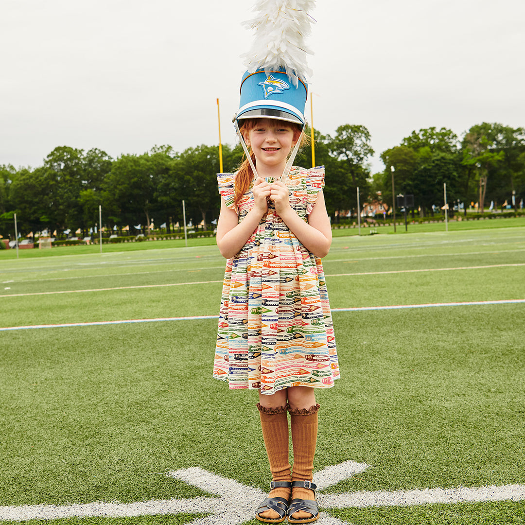 Young girl in a colorful dress holding a drum on a sports field