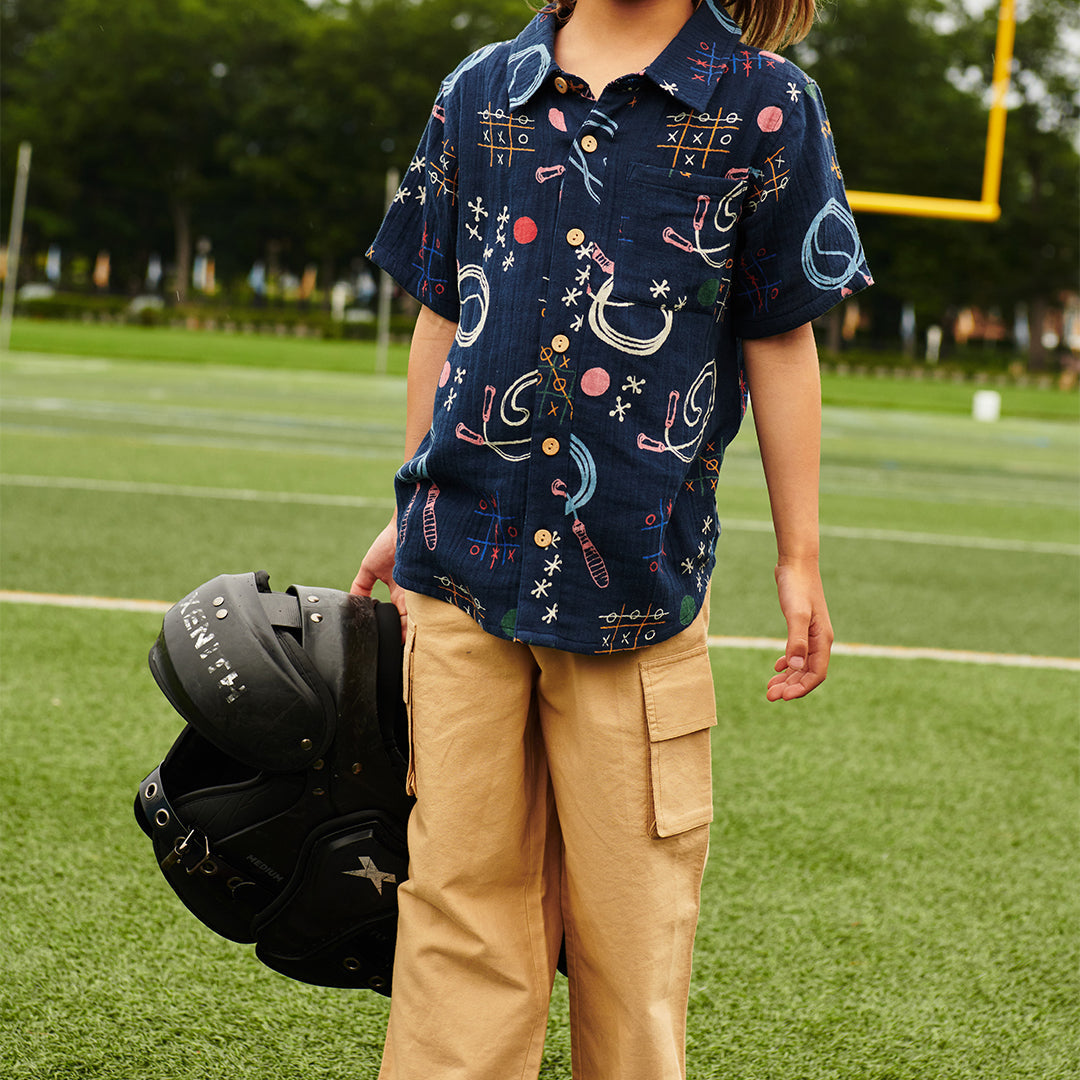 Person wearing a patterned shirt and holding a helmet on a sports field