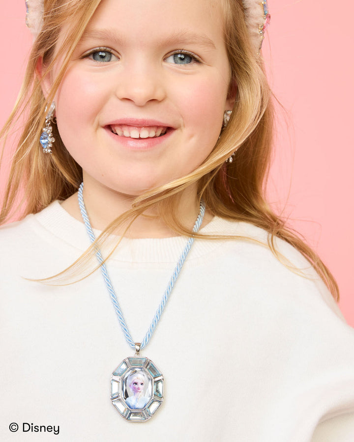 Young girl wearing a necklace with a pendant, against a pink background