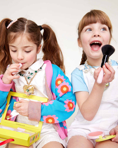 two little girls playing with the elements in the box including the lipstick and blush brush