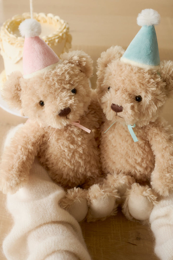 Two teddy bears wearing party hats sitting on a white blanket.