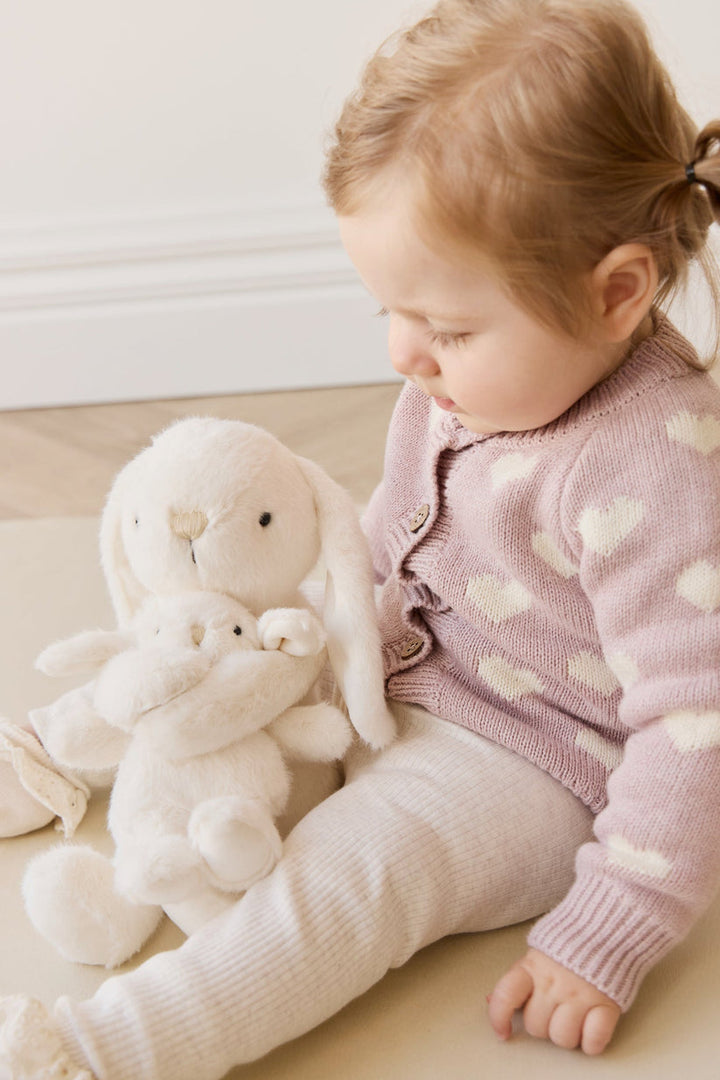Child in a pink sweater with a plush toy on a light surface
