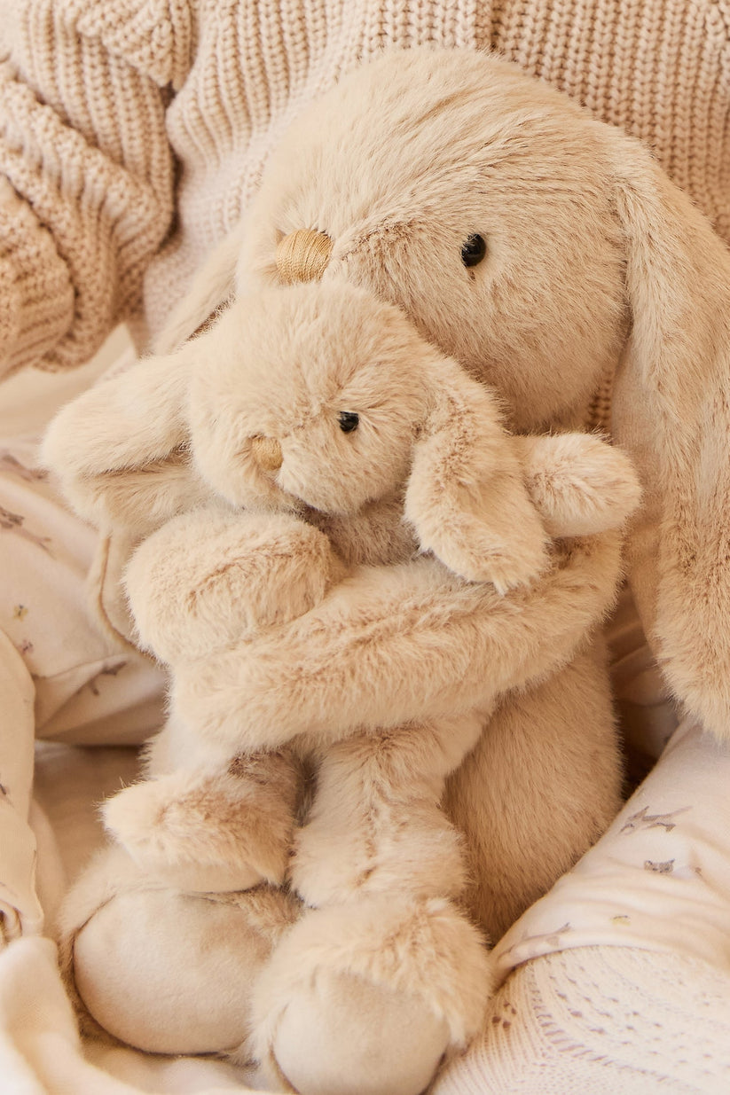 Two beige plush toys hugging each other on a soft textured background