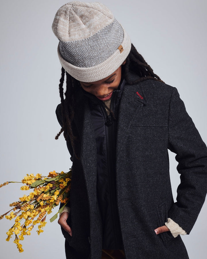 Person wearing a gray coat and patterned beanie holding yellow flowers against a light background