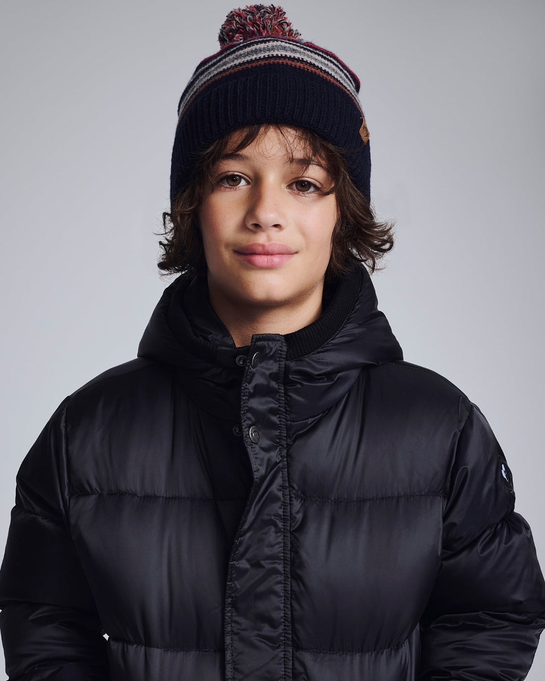 Person wearing a black puffer jacket and striped beanie on a gray background