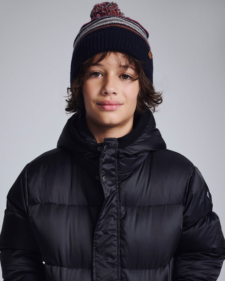 Person wearing a black puffer jacket and striped beanie on a gray background