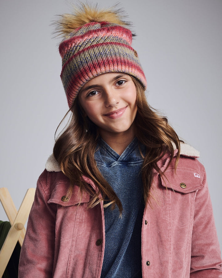 Young girl wearing a colorful knit hat and pink jacket against a gray background