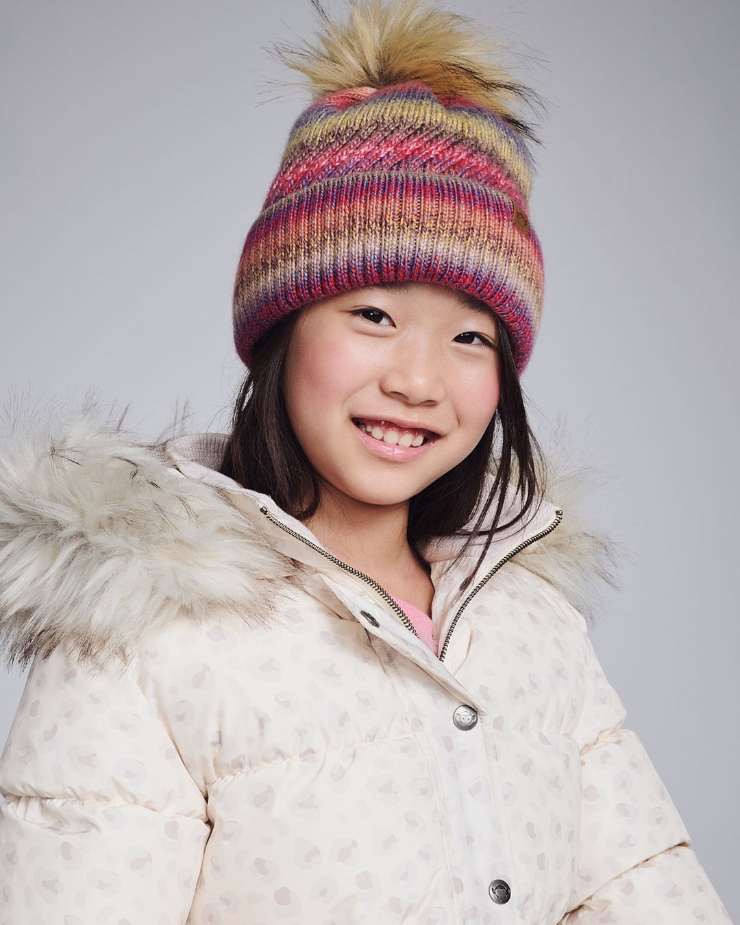 Child wearing a colorful striped beanie and white winter coat on a plain background