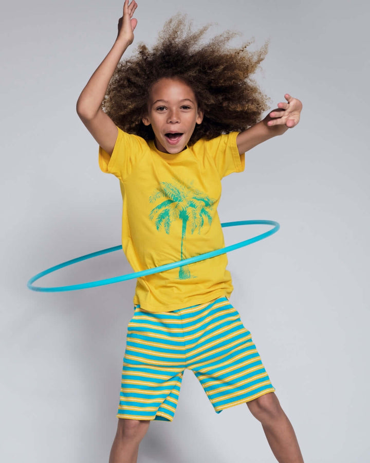 Child in yellow shirt and striped shorts with a blue hula hoop on a gray background