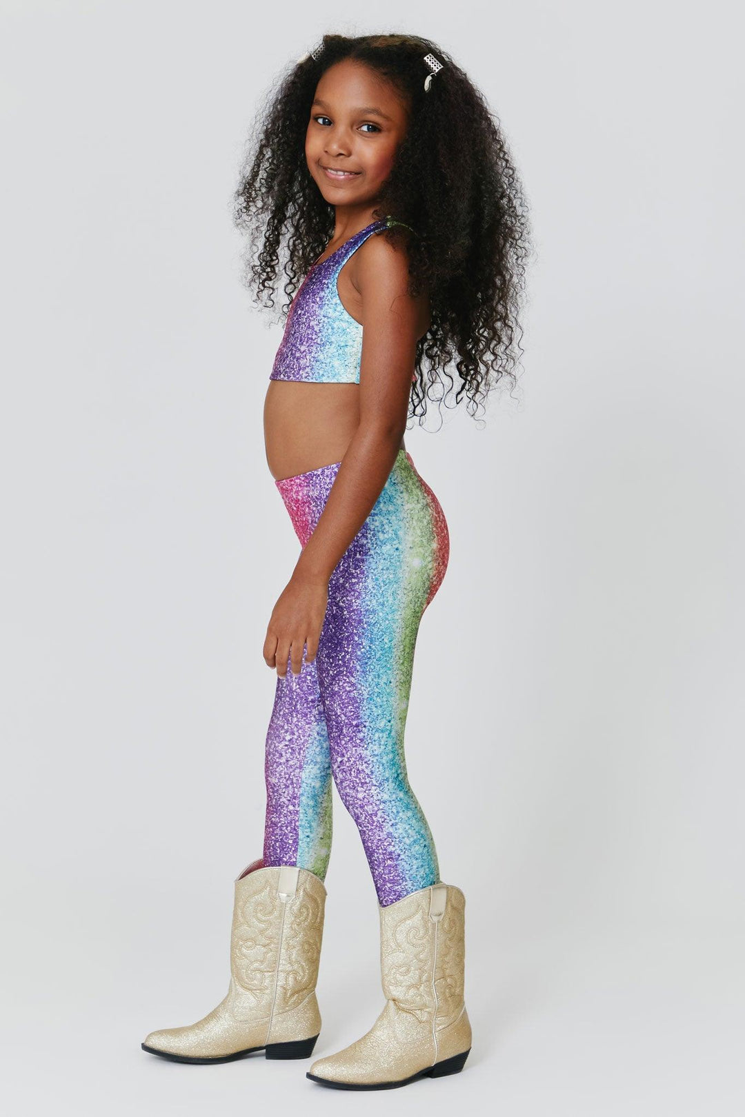 little girl posing from the side in multiglitter leggings: pink, purple, blue and green. 