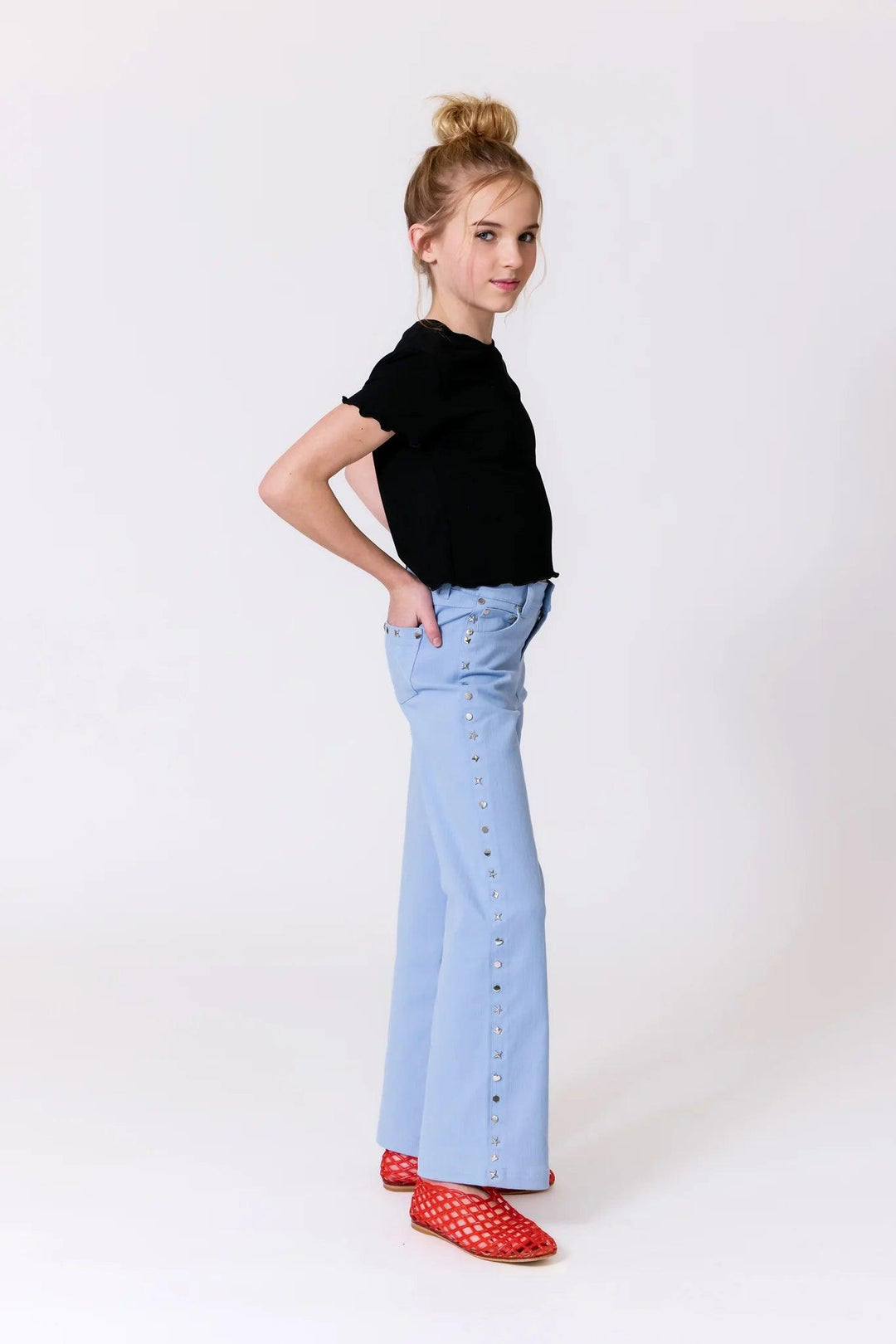 young girl modeling the loose fit, white leg twill pants with studs along the side. 