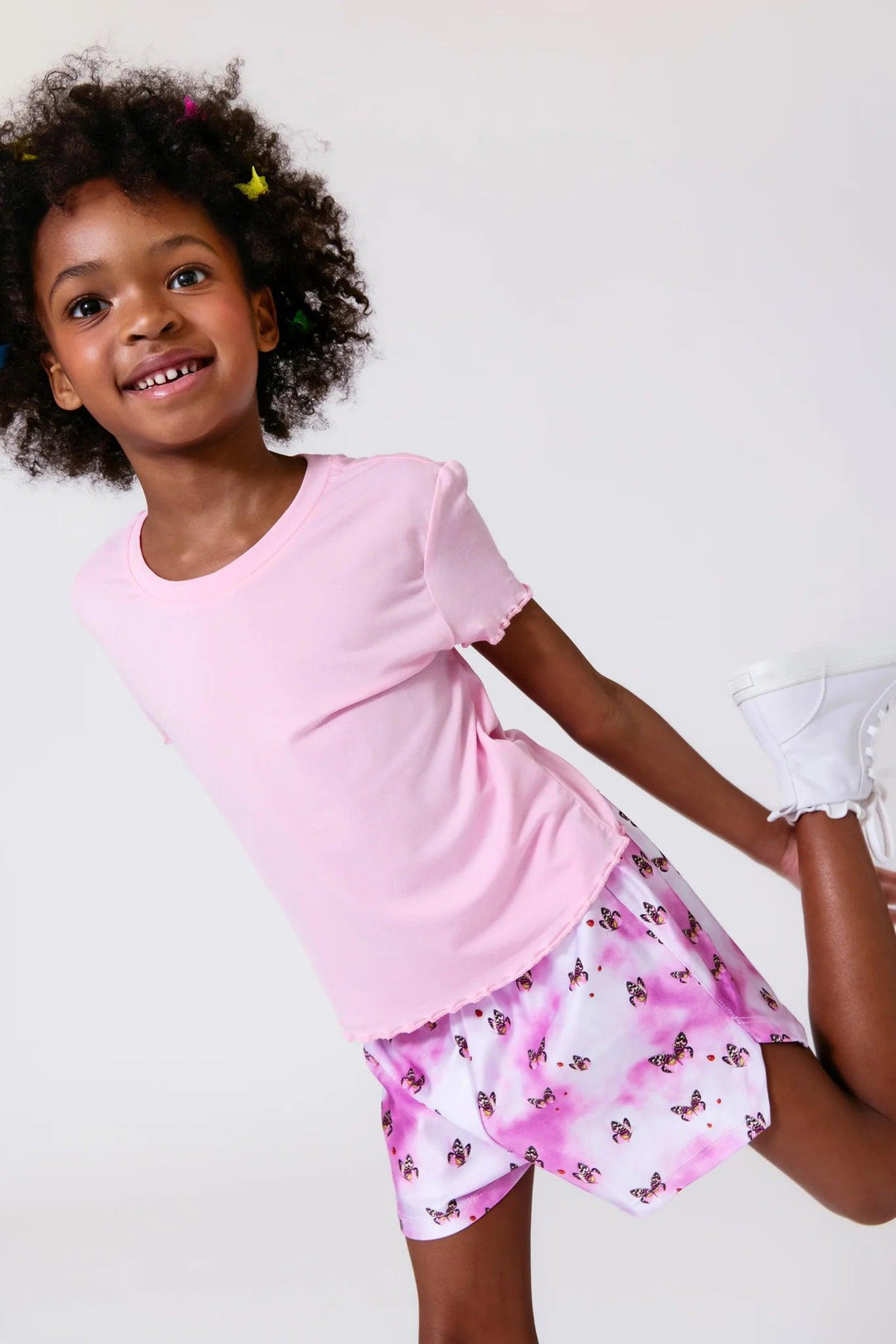 young girl wearing purple swirl shorts with butterflies all over them. the shorts hit mid-thigh. 