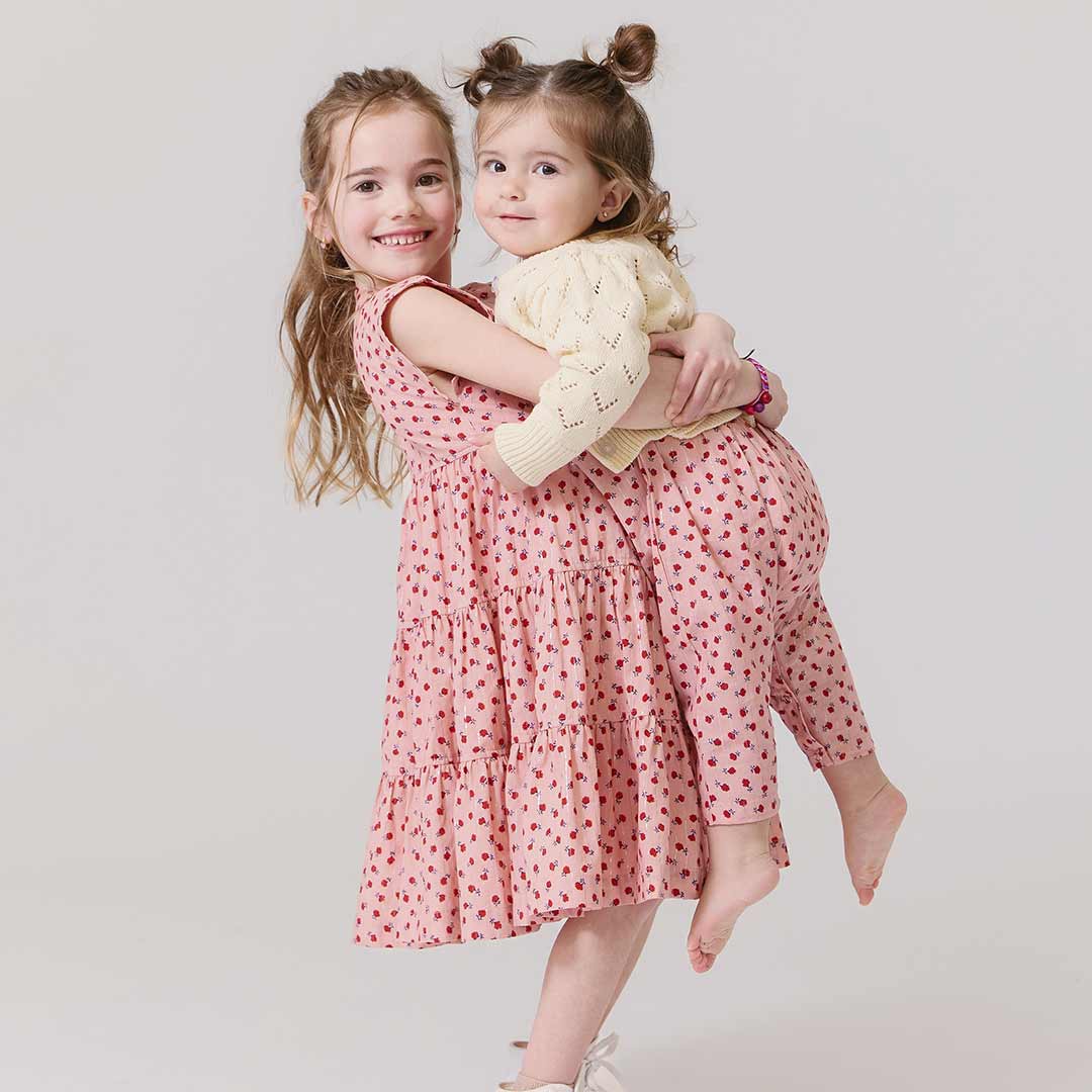 Two young girls in pink dresses and tiny red flowers with red patterns hugging 