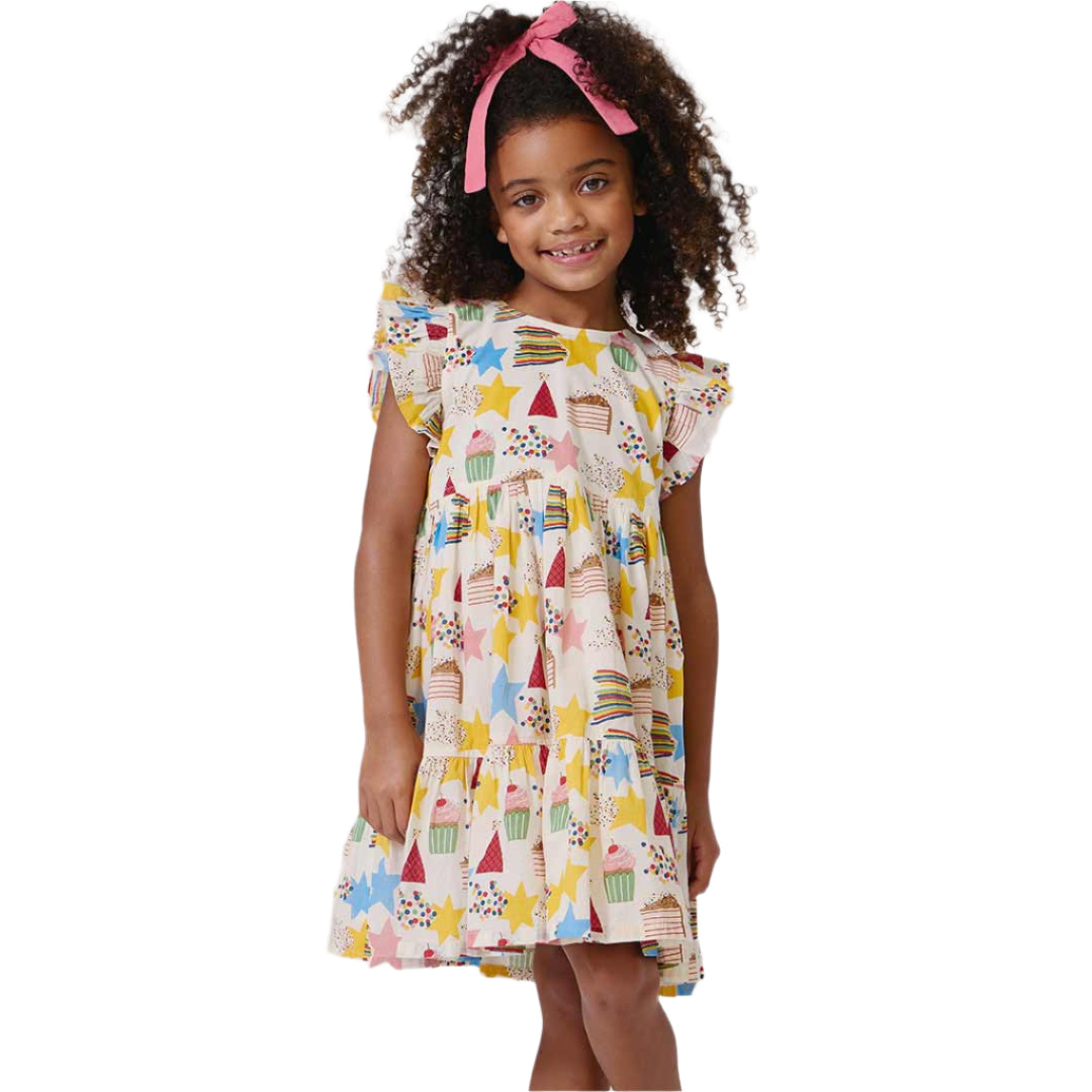 Young girl wearing a colorful dress with star, moon, and birthday cake pattern