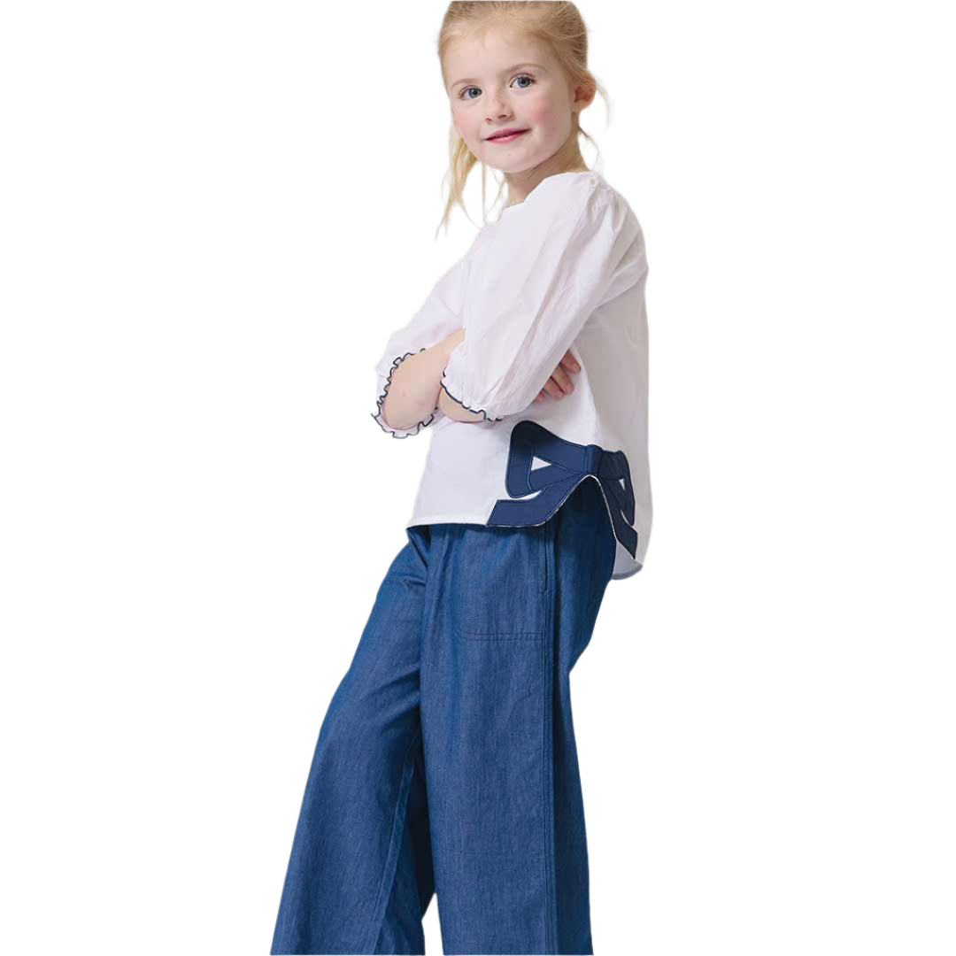 Young girl wearing a white blouse with a blue bow design and blue pants 