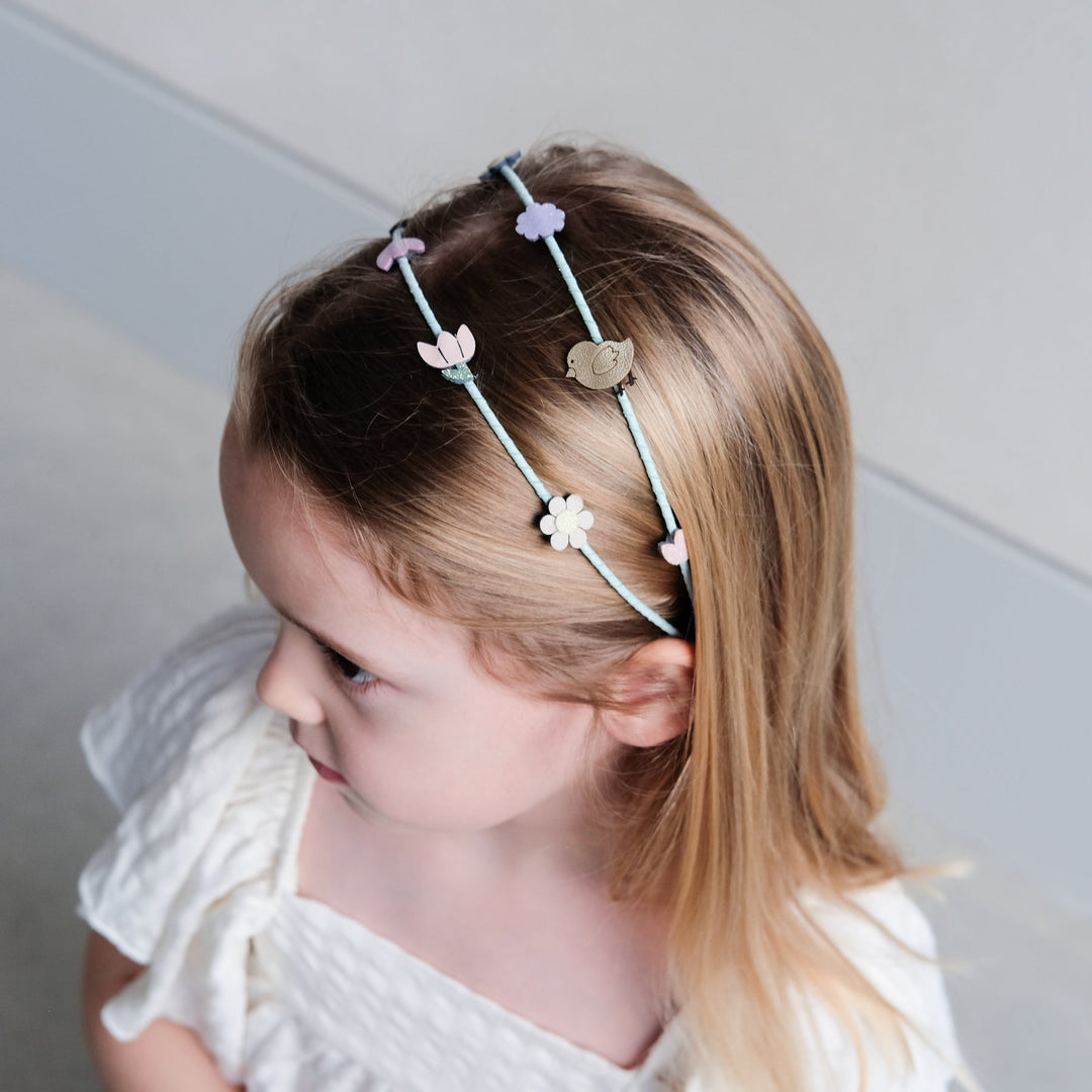 Young girl wearing a decorative headband with floral designs against a neutral background