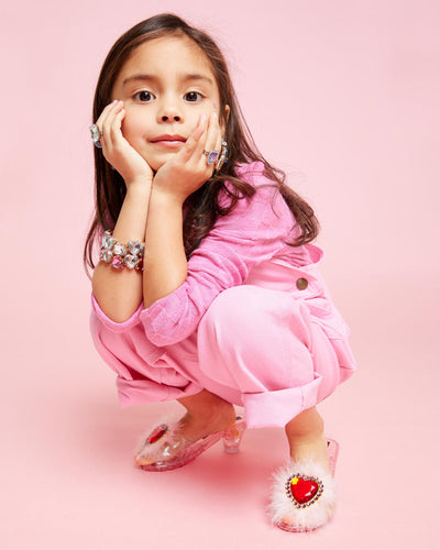 little girl modeling the pink dress up shoes showing how the girl will have room in the shoe as she sits and walks. The feather and red stone are a dominant part of the design. 