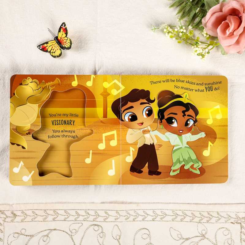 A children's wooden puzzle book featuring a colorful illustration of a boy and girl dancing on a golden stage, with text and musical notes. The book is displayed on a white fabric background with a butterfly decoration on the left and pink roses on the top right.