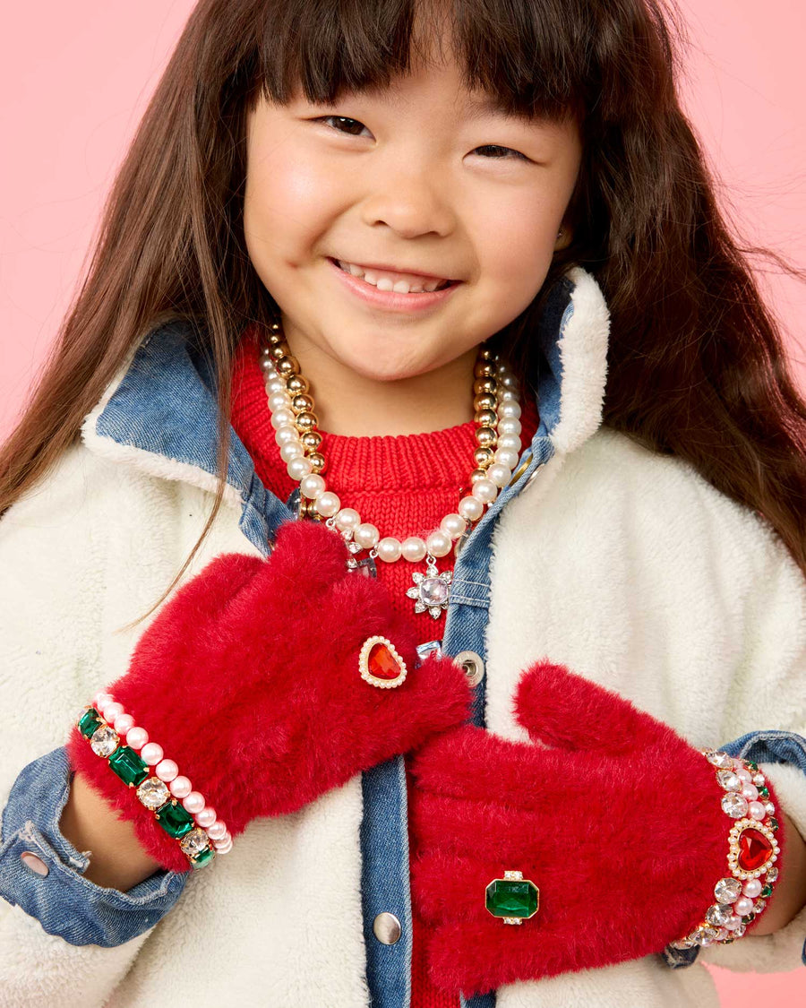 Child wearing red mittens with decorative elements against a pink background
