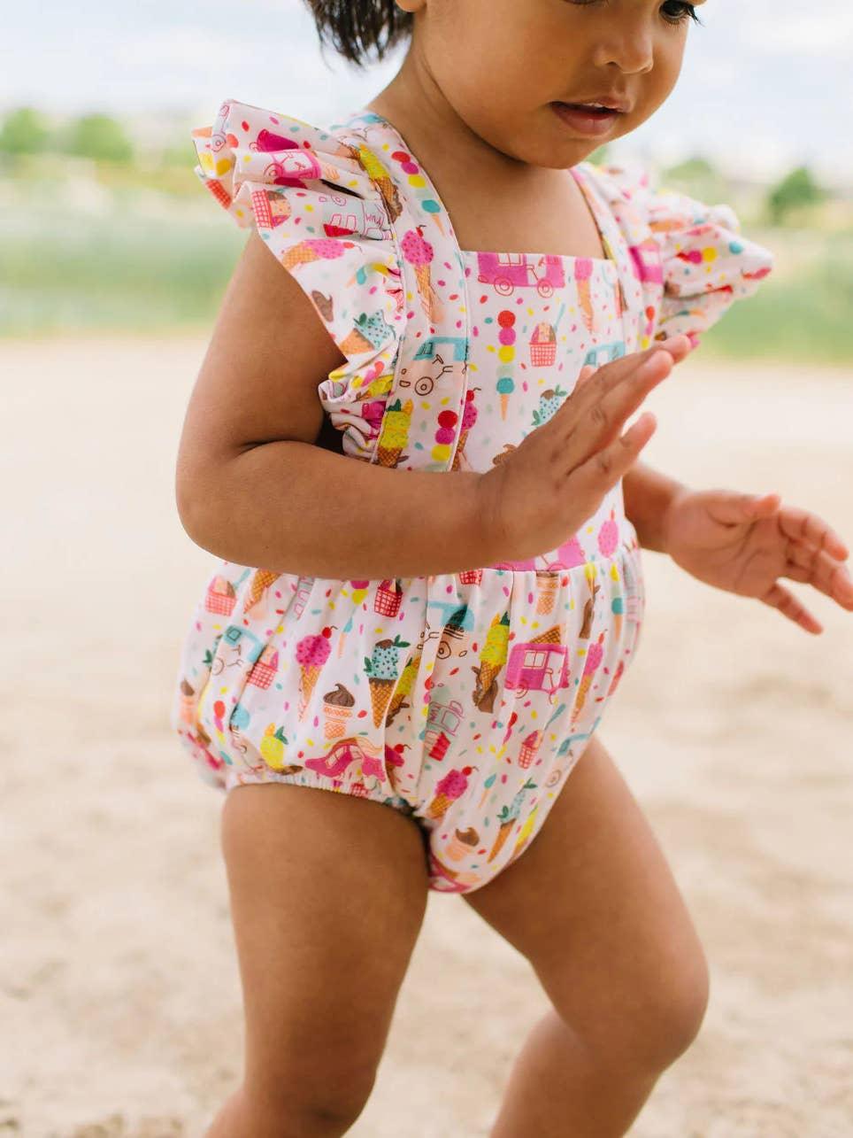 baby wearing a bubble with criss cross straps and ruffles at the sleeves and snaps at the bottom. 