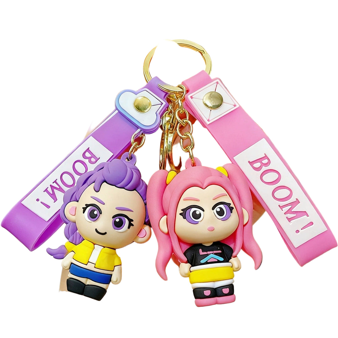 Two colorful keychains with cartoon characters held in a hand, with 'BOOM!' text on a blurred indoor background.