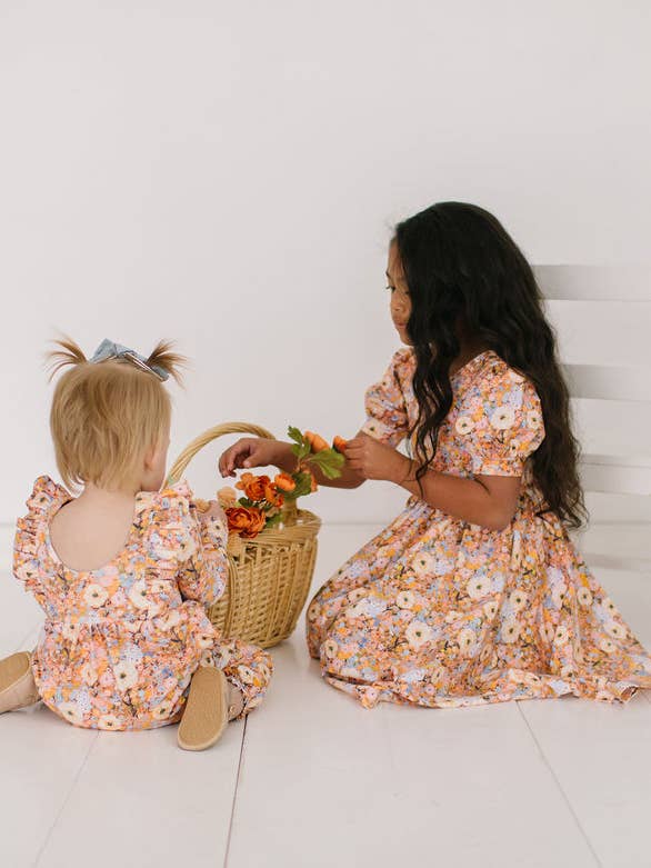 Woman and child in floral dresses with a basket of flowers on a white floor.