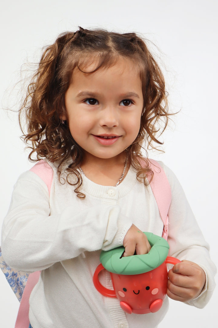 Child holding a red snack cup with a green lid against a white background