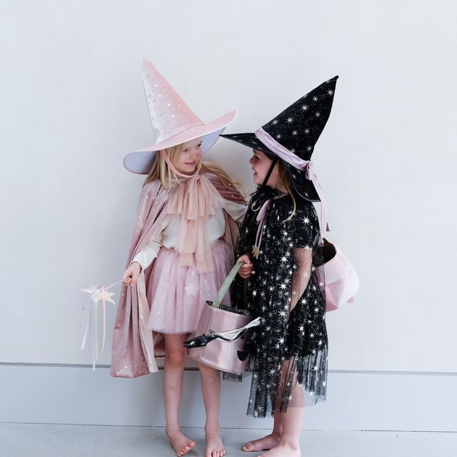 Two children in witch costumes with hats against a white background