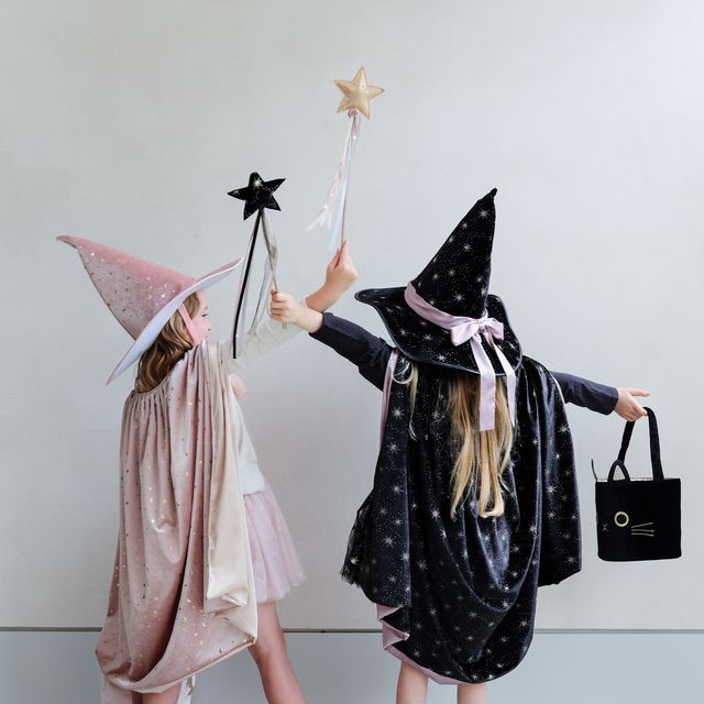 Two children in witch costumes with star-themed accessories on a plain background