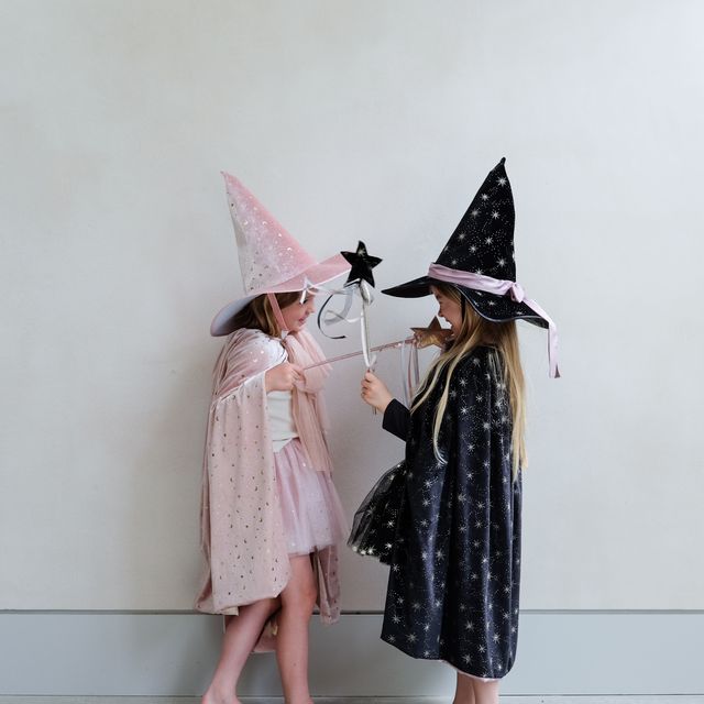 Two children in witch costumes with hats against a plain background