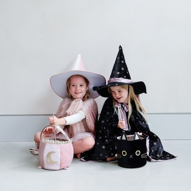 Two children in Halloween costumes with witch hats and candy buckets on a light background