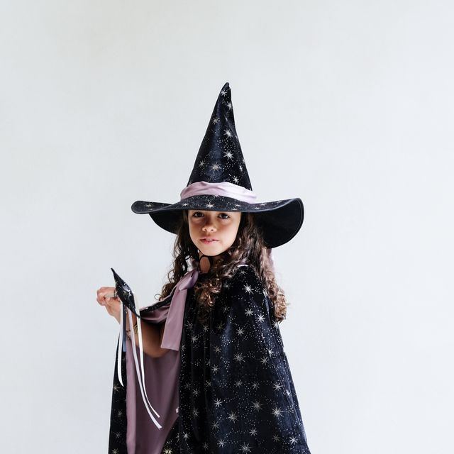 Child wearing a witch hat and cape with star pattern on a plain background