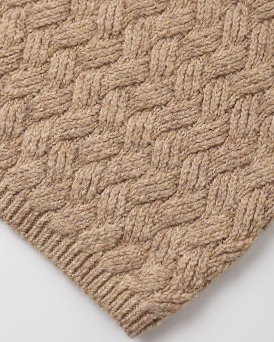 Close-up of a woven textile with a braided basketweave pattern in a warm beige/tan color, showing the texture and ribbed edge on a light neutral background.