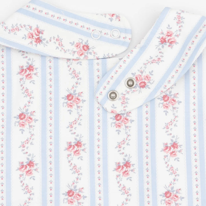 Close-up of a baby garment or textile with a white base, light blue vertical stripes, and pink floral prints. The fabric has a soft texture and is shown folded with metal snap buttons visible.