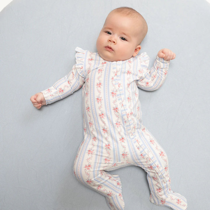 A baby lying on their back wearing a footed long-sleeve jumpsuit with vertical blue stripes and a small pink floral pattern, set against a light blue background.