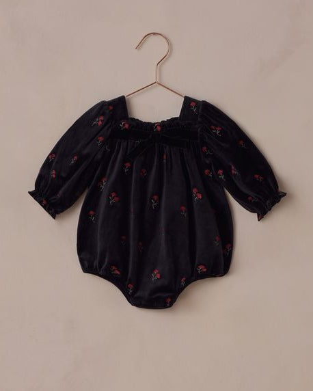 Black baby romper with red patterns on a beige hanger against a beige background